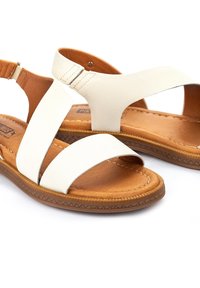 Sandales blanches en cuir à bout ouvert avec semelles intérieures marron rembourrées et brides arrière ajustables sur fond blanc.