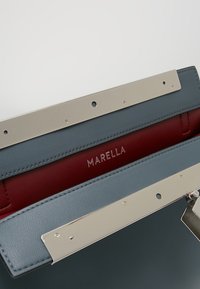 Handväska med grå läderexteriör, röd foder och silverfärgad metallutrustning. Har ett lås på framsidan och präglad "MARELLA" logo.
