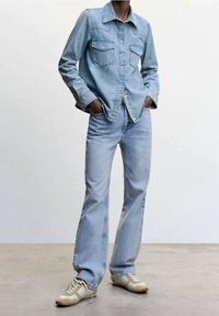 Hellblaues Denimhemd mit zwei Brusttaschen, Knopfdesign, kombiniert mit hellblauen Jeans und cremefarbenen Sneakers mit braunen Akzenten.