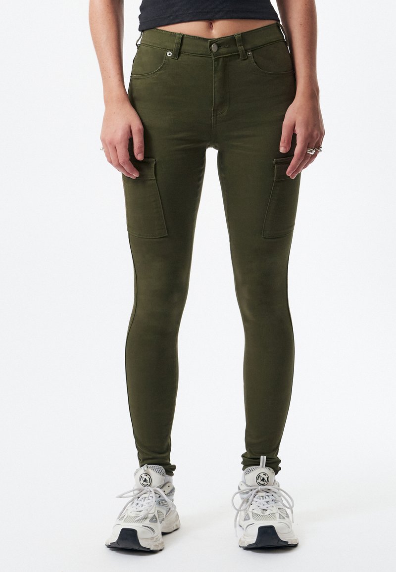 Leggings cargo verde oliva con una forma ajustada, que cuentan con dos bolsillos laterales y sutiles detalles de costura, combinados con zapatillas deportivas blancas.