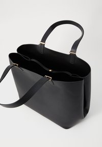 Czarna skórzana torba na ramię z dwoma długimi uchwytami, złotymi elementami ozdobnymi oraz otwartym górnym designem z dwoma wewnętrznymi przegródkami.