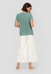 Miętowa koszulka na krótki rękaw w połączeniu z białymi spodniami o szerokich nogawkach i beżowymi sandałami, charakteryzująca się luźnym krojem i miękką teksturą materiału.