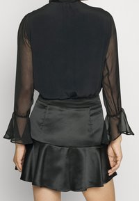 Black blouse with sheer long sleeves and ruffle cuffs, paired with a flared black satin mini skirt featuring a smooth texture and waist seam.