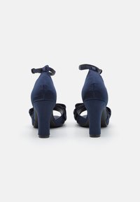 Navy blue high-heeled shoes with satin finish, rounded toe, ankle strap, and decorative ruffled accents on the front.