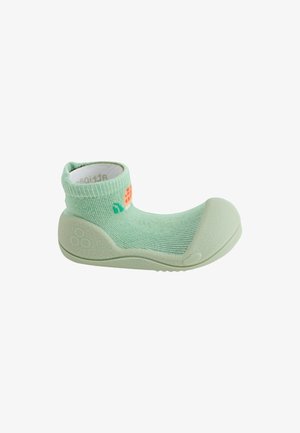Scarpa morbida verde per bambino con tomaia tipo calzino e suola e punta in gomma protettiva, con piccolo disegno arancione e verde sul lato.