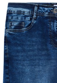 Jeans di denim blu scuro in primo piano che mostrano la tasca anteriore, la tasca porta monete, il passante per cintura e il bottone in metallo con cuciture a contrasto.