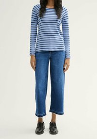 Modrý a bílý pruhovaný top s dlouhým rukávem, doplněný o tmavě modré džíny s širokými nohavicemi a černé šněrovací boty s třepeným lemem.