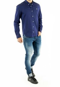 Mörkblå skjorta med krage, kombinerad med ljusblå jeans och svarta sneakers. Outfitten har en figurnära design och kontrasterande texturer.