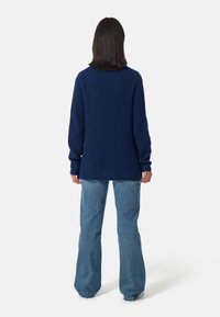 Maglione a coste di colore blu navy con maniche lunghe e scollatura rotonda, abbinato a jeans a zampa d'elefante di colore blu chiaro. Il maglione ha una vestibilità comoda e spacchi laterali.