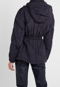 Dunkelviolette Daunenjacke mit Kapuze, taillierter Optik und gestepptem Muster. Verfügt über elastische Bündchen und einen lässigen Schnitt.