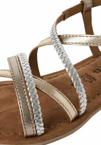 Sandali con cinturini che presentano una lavorazione in oro e argento metallizzato su una soletta in suede marrone, con suola piatta e design minimale.