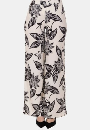 Pantaloni color crema a gamba larga con stampa floreale e foglie nere, indossati con scarpe nere con punta appuntita.