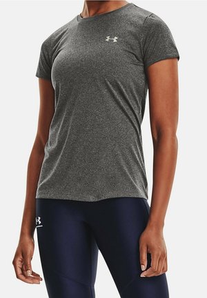 Person trägt ein eng anliegendes, dunkelgraues, kurzärmeliges Sportshirt und marineblaue Leggings, steht mit entspannten Armen an den Seiten.