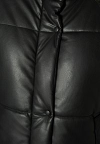 Černá kožená zateplená bunda s prošívaným designem, kulatými knoflíky a hladkou texturou. Zdůrazňuje teplo a strukturovaný tvar.