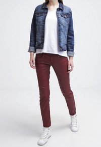 Jeansjacka med blå stone wash, vit t-shirt, röda slim-fit byxor och vita sneakers. Funktioner inkluderar knappar och uppvikta ärmar på jackan.