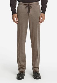 Jasnobrązowe spodnie o miękkim, teksturowanym wykończeniu. Posiadają elastyczny pas z troczkami oraz boczne kieszenie. Połączone z czarnymi butami.