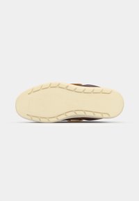 Brun og gul sneakersåle med en teksturert hvit gummisåle, med bølgemønster og dype mønstre for grep.