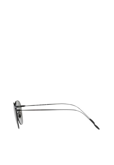 Occhiali da sole rotondi con lenti scure, montatura sottile in metallo nero e stanghette sottili. Presentano un design minimalista senza loghi visibili.