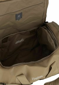 Bolsa de deporte en tela beige con un interior espacioso, bolsillo con cremallera y logo de la marca. Presenta asas resistentes y un cierre de cremallera suave.