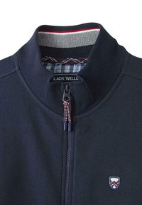 Veste zippée bleu marine avec un col montant, dotée d'un intérieur rayé coloré, d'une fermeture éclair à l'avant et d'un petit écusson brodé sur la poitrine gauche.