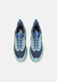 Trailrunning-Schuhe in einem dunklen Blau und hellen Grün, mit einem Obermaterial aus Mesh, einer strukturierten Sohle und reflektierenden Akzenten.