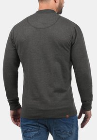 Mørkegrå crewneck sweatshirt med lange ærmer, struktureret stof, ribbede manchetter og kant, med et lille mærketikette nær bunden.