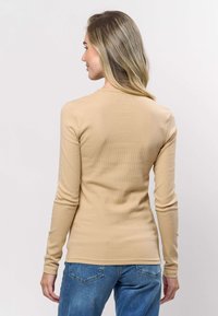 Ljusbeige långärmad ribbad topp med rund halsringning. Slät textur, figurnära design, kombinerad med blå jeans i denim.