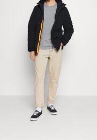 Svart zip-up jacka med orange foder, grå t-shirt, beige byxor och svarta sneakers med vita sulor. Har huva och fickor.