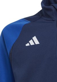 Marineblauw sporttop met lichtblauwe accenten, hoge kraag, rits en wit logo. Soepele textuur, actieve pasvorm, zonder patronen of metalen onderdelen.