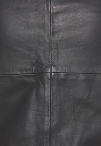 Texture de cuir noir avec une finition lisse, présentant des lignes de couture distinctes formant un motif carré sur toute la surface.