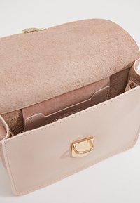 Una borsa morbida di colore rosa, parzialmente aperta, rivela un interno in feltro con un compartimento per le carte. La borsa presenta una chiusura dorata e dettagli di cucitura.