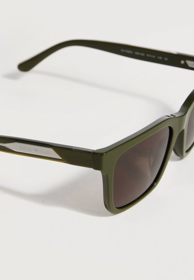 Mat olijfgroene rechthoekige zonnebril met donker getinte glazen en dunne pootjes, met een subtiel merklogo aan de zijkant.