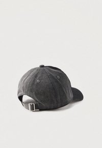 Tumši pelēka džinsa beisbola cepure ar regulējamu metāla sprādzi, redzama no aizmugures uz vienkārša gaiša fona.