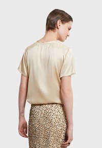 Krémová saténová blúzka s krátkymi rukávmi, s okrúhlym výstrihom a voľným strihom, skombinovaná s béžovou sukňou s detailmi zlatého leopardieho vzoru.