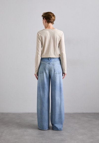 Lightweight beige long-sleeve top paired with loose-fitting, light blue denim wide-leg jeans, featuring back pockets and faded accents.