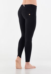 Czarne legginsy wykonane z elastycznego materiału, z wyprofilowanym szwem i małym logo na tylnej kieszeni. Długość do kostek, bez mankietów.
