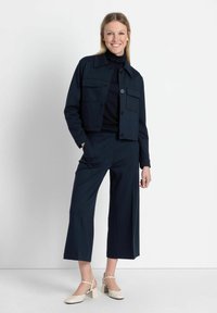 Marineblauwe cropped jas met twee voorzakken, gecombineerd met marineblauwe wijde broek en beige blokhak schoenen. Glad textuur van de stof.