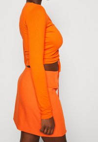 Orange långärmad topp med en figurnära design, kombinerad med en matchande orange minikjol. Båda plaggen har en slät textur och en tajt passform.