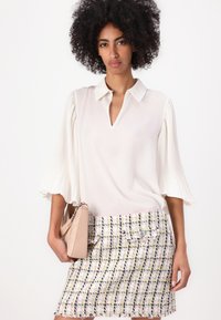 White collared blouse with pleated sleeves, paired with a multicolored tweed skirt. Accessories include a light beige shoulder bag.