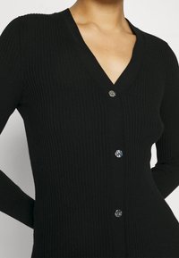 Cardigan nero lavorato a maglia con maniche lunghe, caratterizzato da un colletto a V, una texture a coste e bottoni decorativi argentati lungo la parte anteriore.