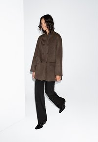 Brown double-breasted wool coat with side pockets, worn over black wide-leg trousers and pointed black heels, showcasing a relaxed fit.