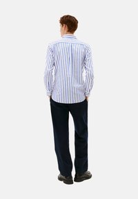 Camicia a maniche lunghe da uomo con righe verticali blu e bianche, colletto con bottoni e una texture di cotone liscia, abbinata a pantaloni scuri.