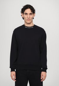 Felpa nera con scollo a girocollo, maniche lunghe, polsini a coste e un logo bianco a contrasto sul colletto. Tessuto morbido.