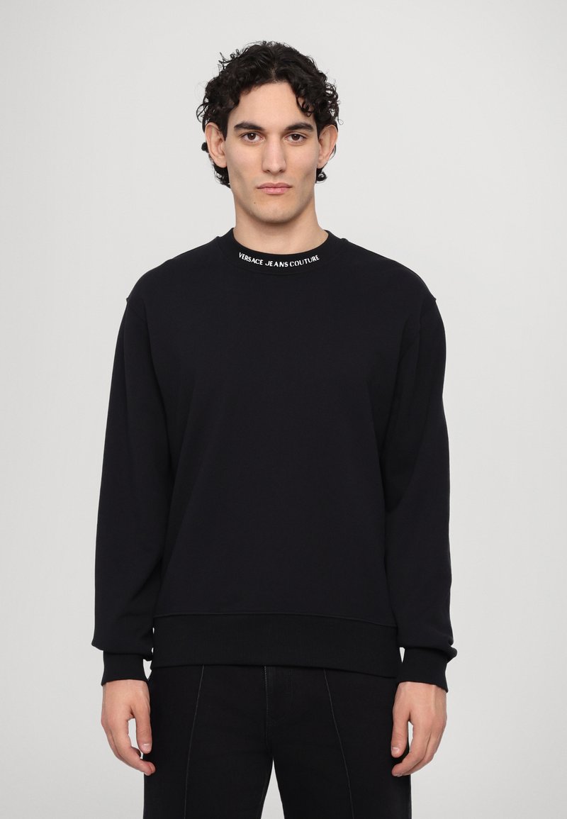 Felpa nera con scollo a girocollo, maniche lunghe, polsini a coste e un logo bianco a contrasto sul colletto. Tessuto morbido.