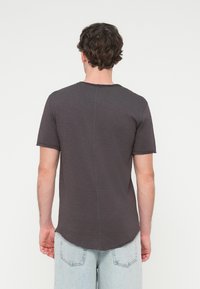 Γκρι κοντομάνικο μπλουζάκι με καμπυλωτό τελείωμα και ορατές ραφές, κατασκευασμένο από υφασμάτινο υλικό με υφή. Προβολή από πίσω.