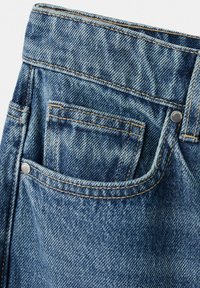 Jean en denim bleu en gros plan montrant une poche avant avec une petite poche à monnaie à l'intérieur, avec des coutures visibles et des rivets métalliques.