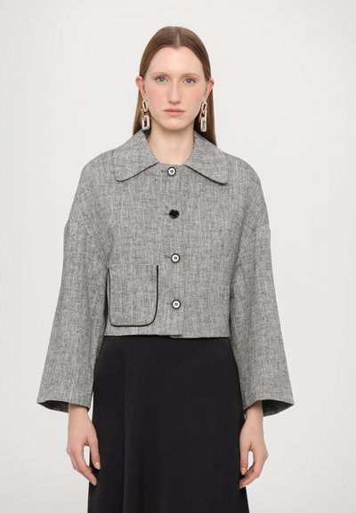 Veste grise texturée raccourcie avec un large col, des boutons noirs et une poche avant, avec des manches tombantes et une silhouette ajustée.