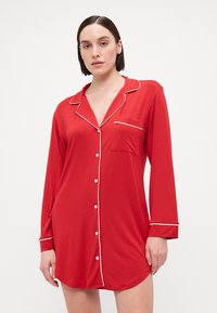 Camisa de noite de algodão vermelho com um corte relaxado, mangas longas, com acabamento branco ao longo do colarinho e do bolso, e fecho frontal com botões.