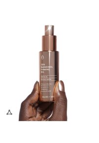 Mano che tiene una bottiglia spray color bronzo con l'etichetta CE15 Bakuchiol Firming Oil con vitamine C, E e altri nutrienti su sfondo bianco.