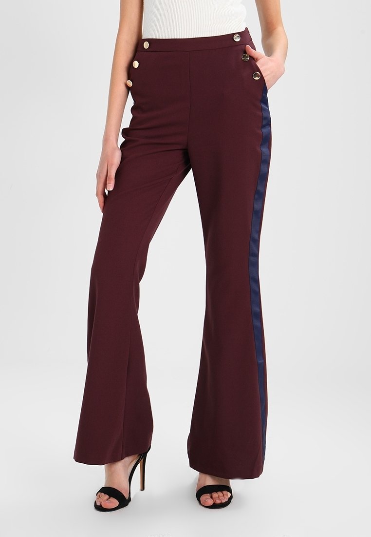 Pantalon taille haute bordeaux avec des accents de boutons dorés, des bandes latérales bleu marine et une coupe évasée. Confectionné dans un tissu lisse et structuré.